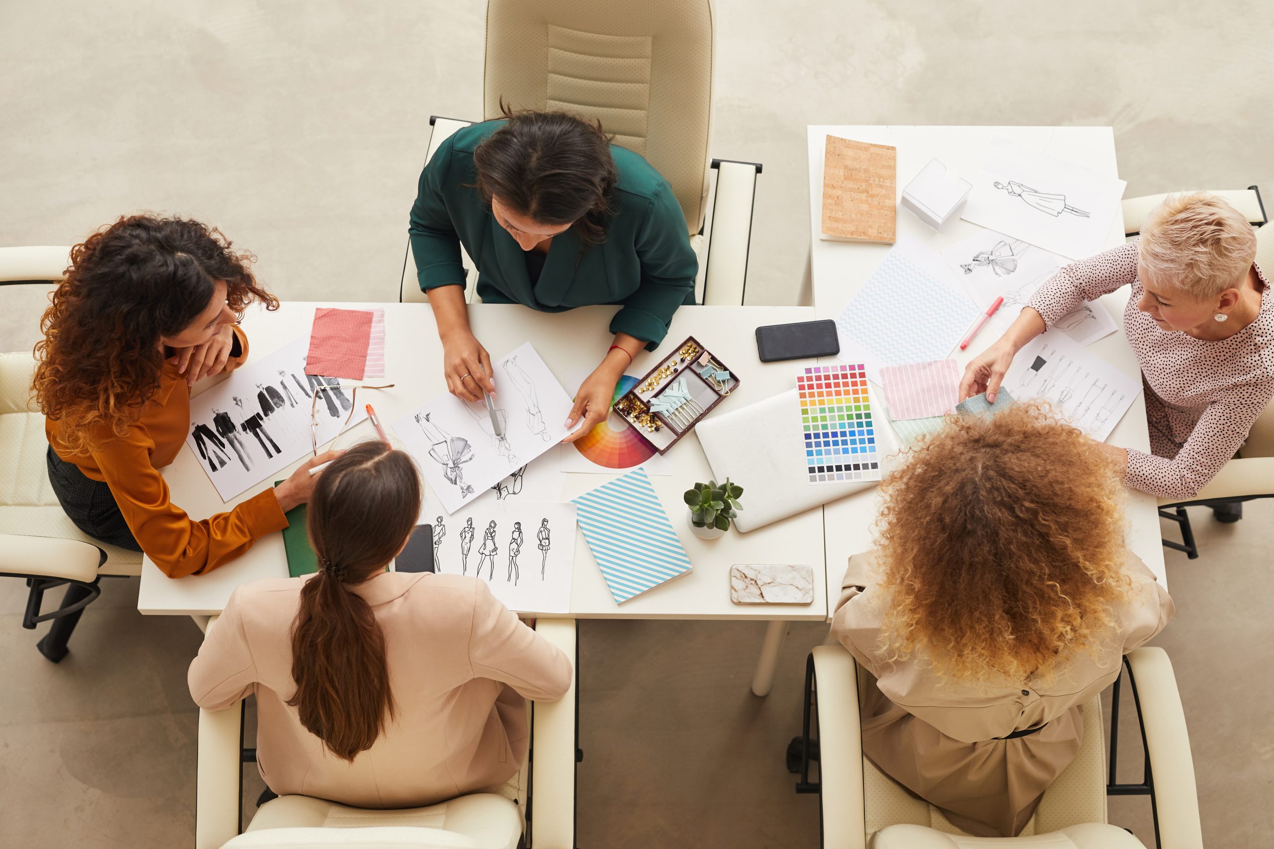 Horizontal from above shot of five stylish women coworking on new clothes design concept
